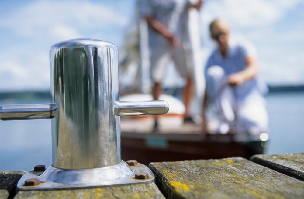 Focus on the mooring bollard as boaters prepare to dock in the background.